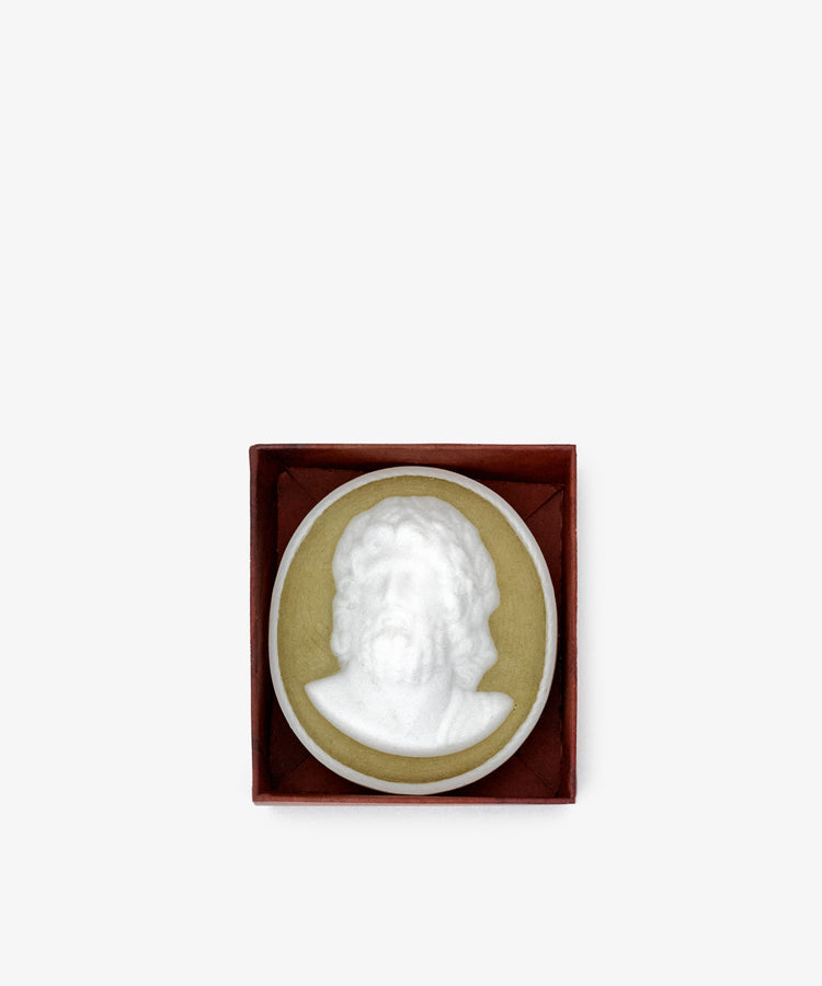 A white cameo brooch depicting a bearded man's bust, inspired by Hercules Soap, is set in a green oval and presented in a brown square box on a plain white background.