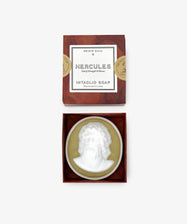A white sculptural Hercules Soap bar with a raised Hercules profile is displayed in an open box, with the lid above reading: 