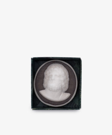 A white relief sculpture of a bearded man’s bust set in a dark round frame, displayed in a small open box—perfect as classical bathroom decor. Inspired by Hercules Soap, hand-poured in London.