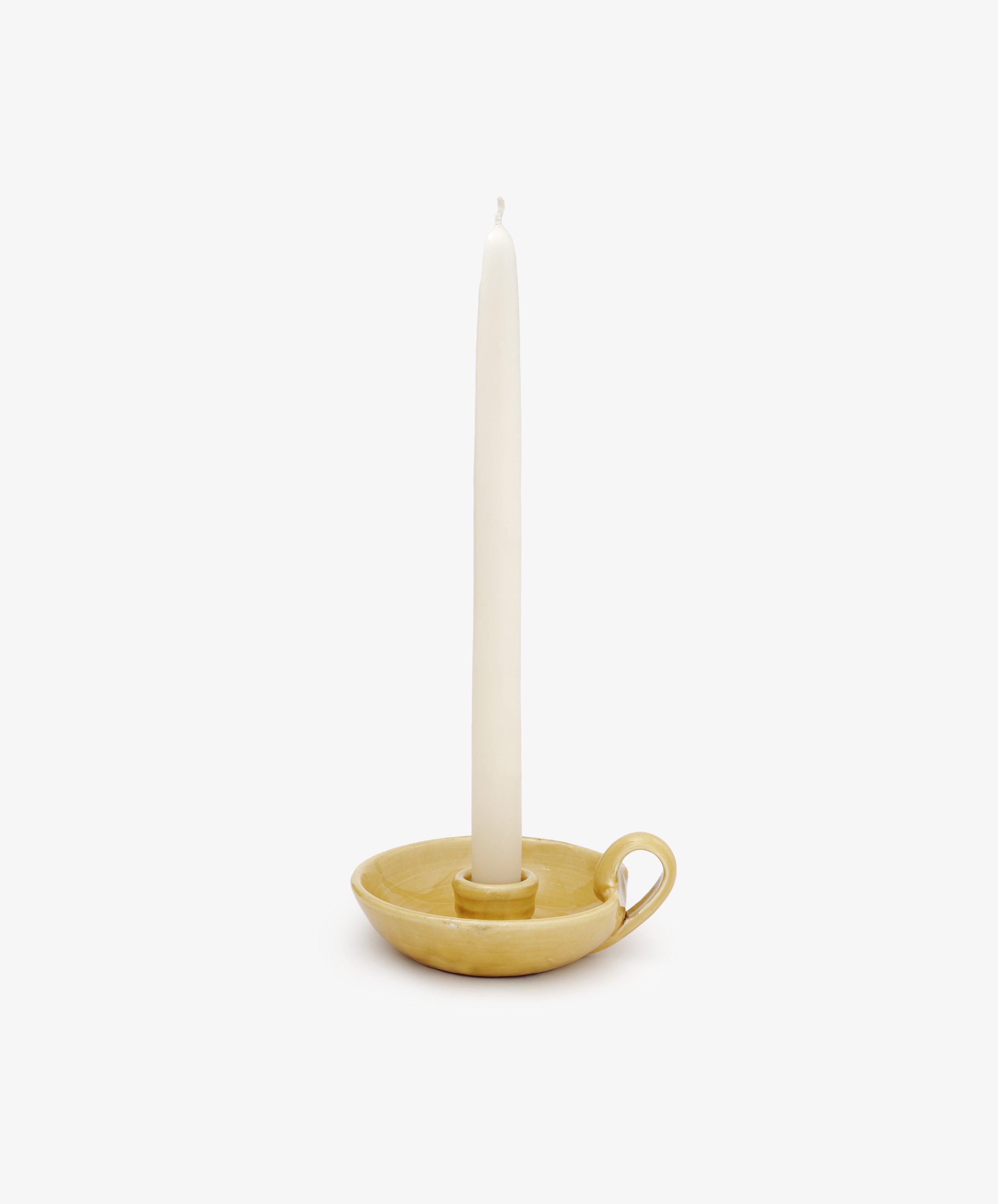 A white tapered candle stands in a yellow ceramic holder with a handle against a plain white background—an ideal touch for your Sparks Flying Bundle this Valentine’s Day.