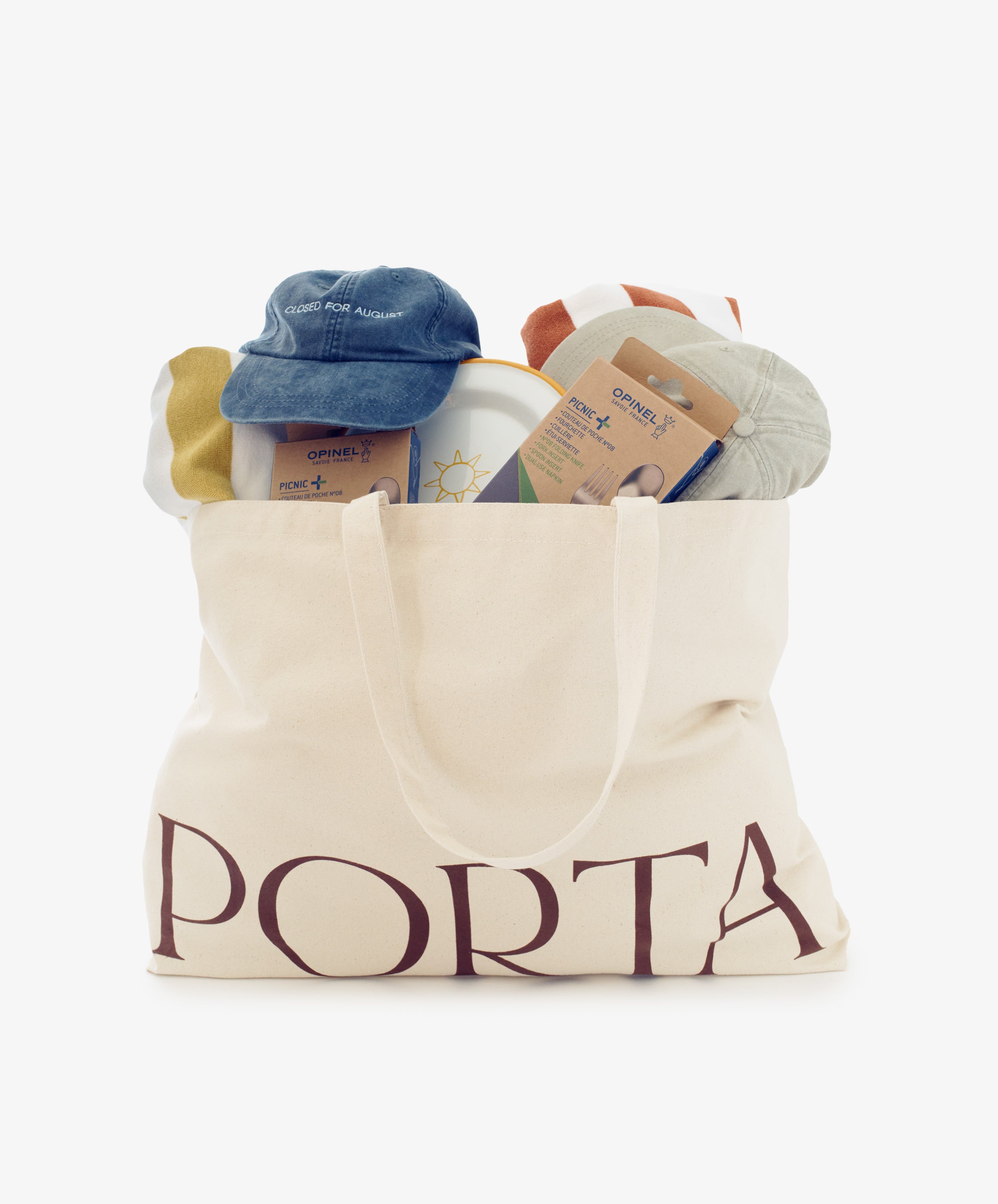 The Sole Weekender is a canvas tote filled with summer beach essentials—two baseball caps, packaged socks, towels, a bottle, and picnic cutlery—all neatly arranged and visible above the bag’s opening.