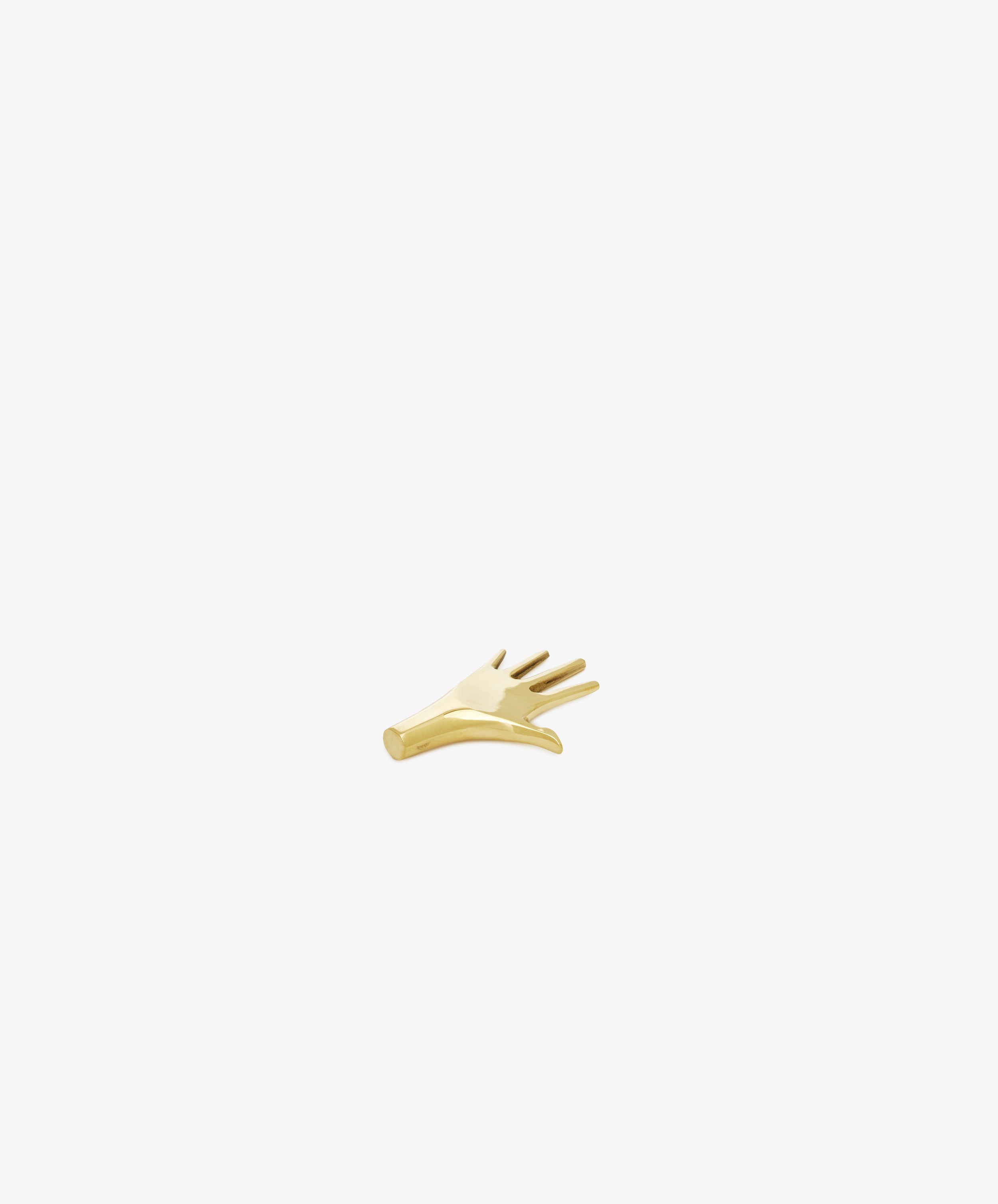 The Hand Paperweight, inspired by Viennese modernism, is a small gold object shaped like a hand with five outstretched fingers, designed to serve as a sculptural paperweight on any desktop.
