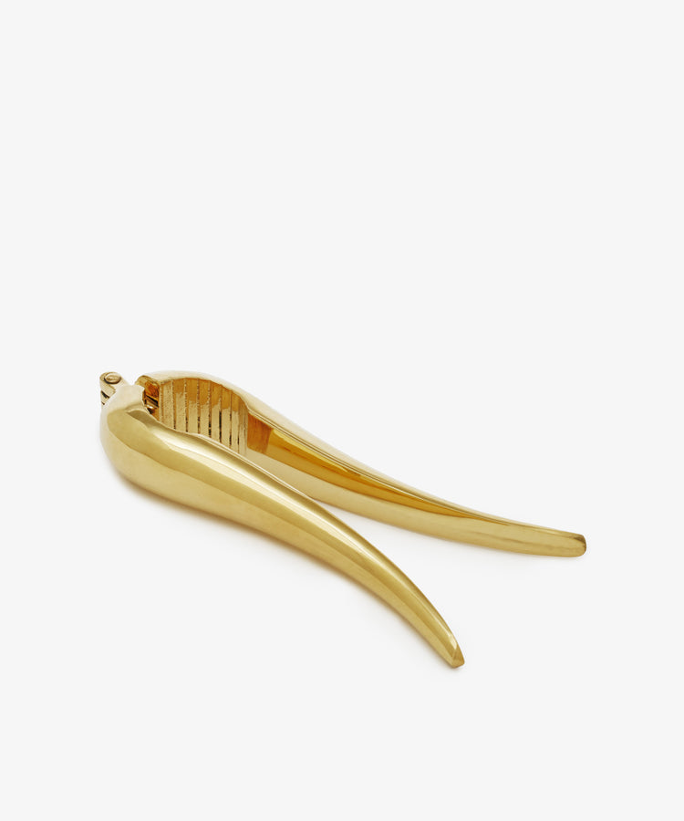 A gold-colored metal Nutcracker with a sleek, curved design, reminiscent of a modern garlic press, is displayed on a white background.