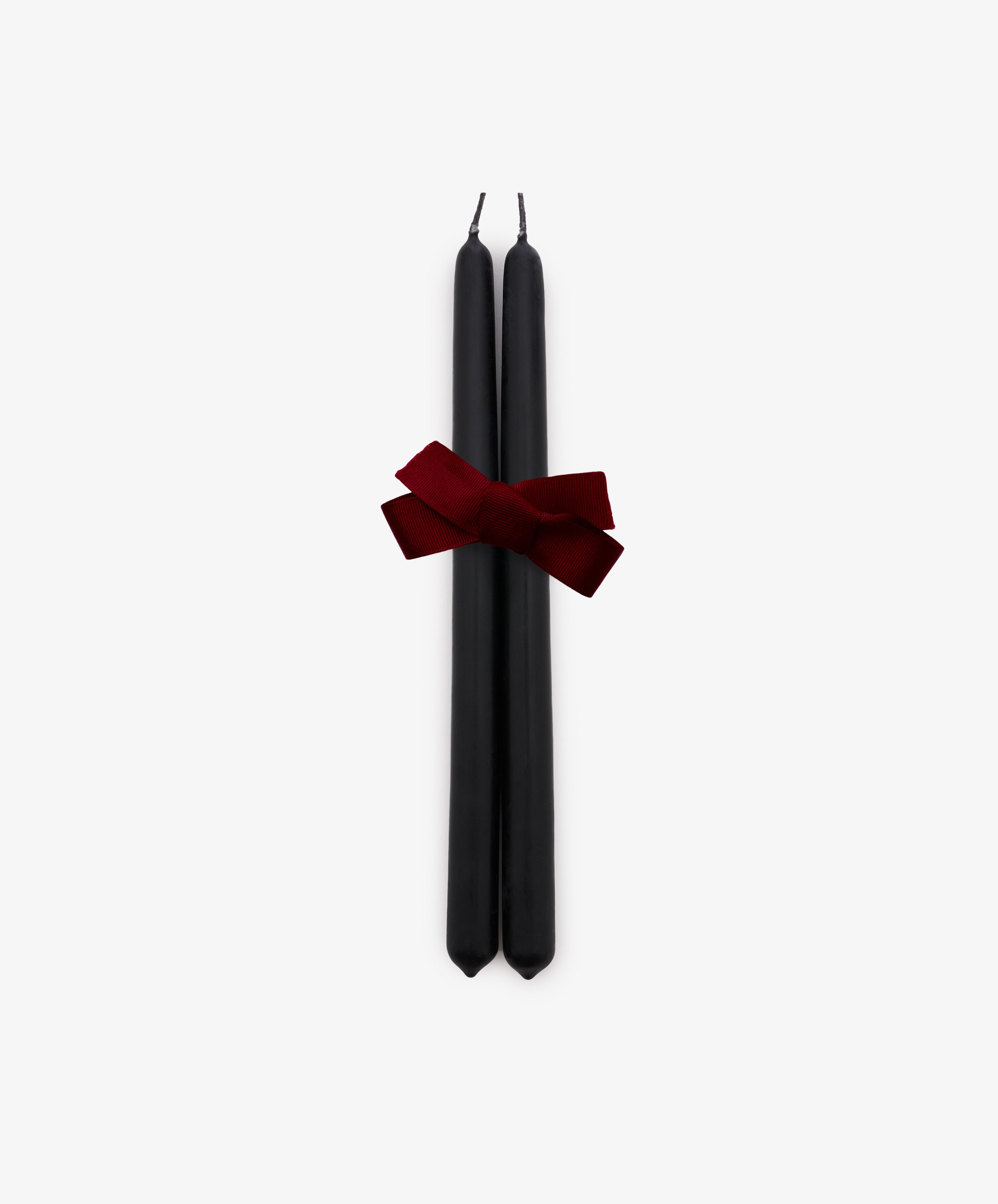 A set of two Tapered Candles in matte black are elegantly bound with a dark red ribbon and displayed against a plain white background. Hand-dipped for quality, these candles combine sophisticated style with a long burn time, making them ideal for any occasion.