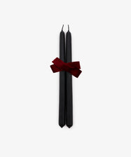 A set of two Tapered Candles in matte black are elegantly bound with a dark red ribbon and displayed against a plain white background. Hand-dipped for quality, these candles combine sophisticated style with a long burn time, making them ideal for any occasion.