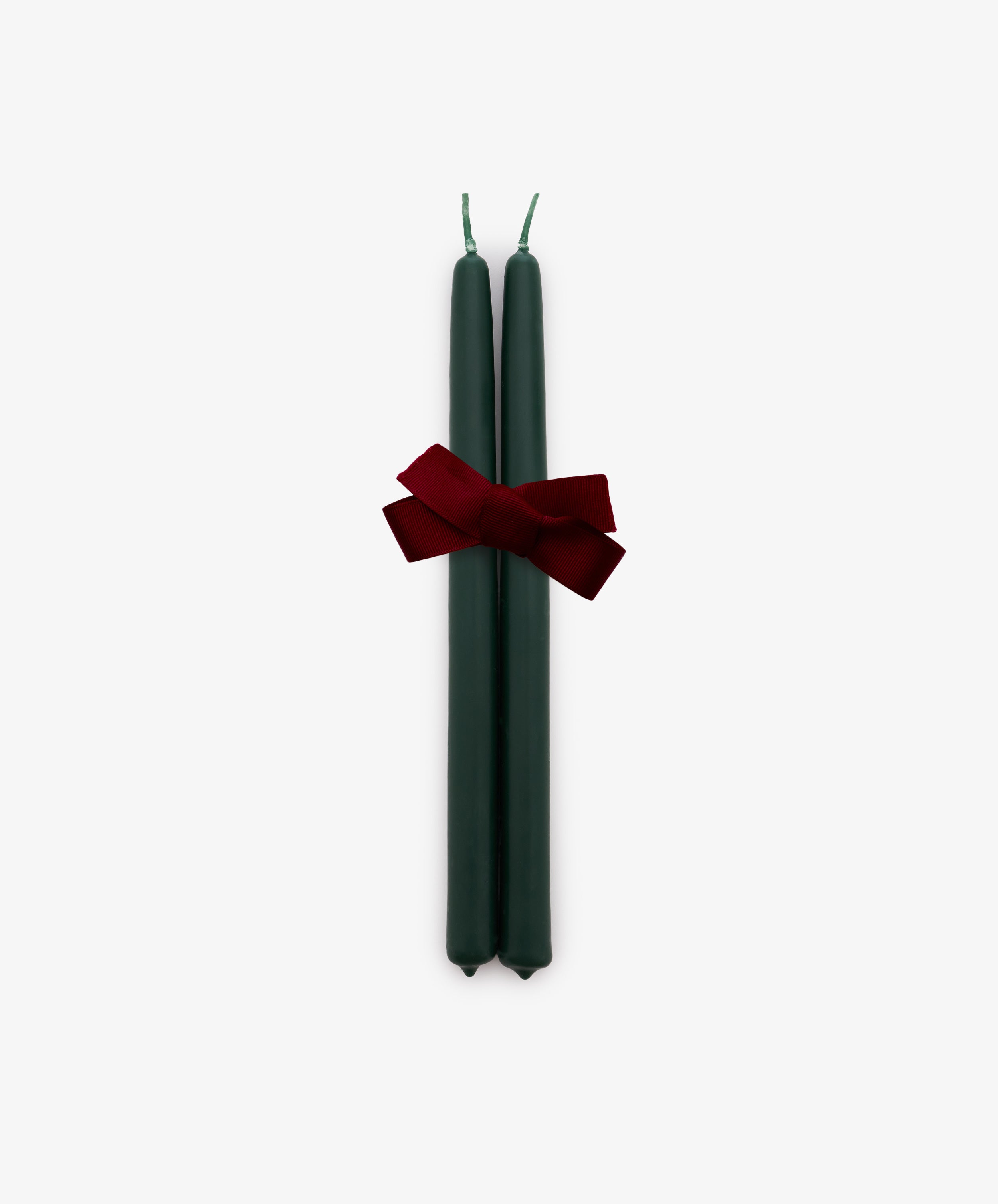 A set of two Tapered Candles in forest green, hand-dipped and tied together with a red bow, is displayed against a plain white background.