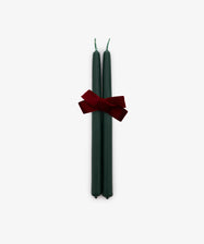 A set of two Tapered Candles in forest green, hand-dipped and tied together with a red bow, is displayed against a plain white background.