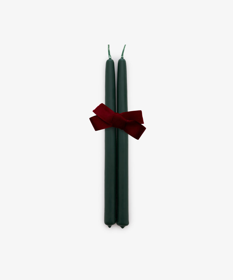 A set of two Tapered Candles in forest green, hand-dipped and tied together with a red bow, is displayed against a plain white background.