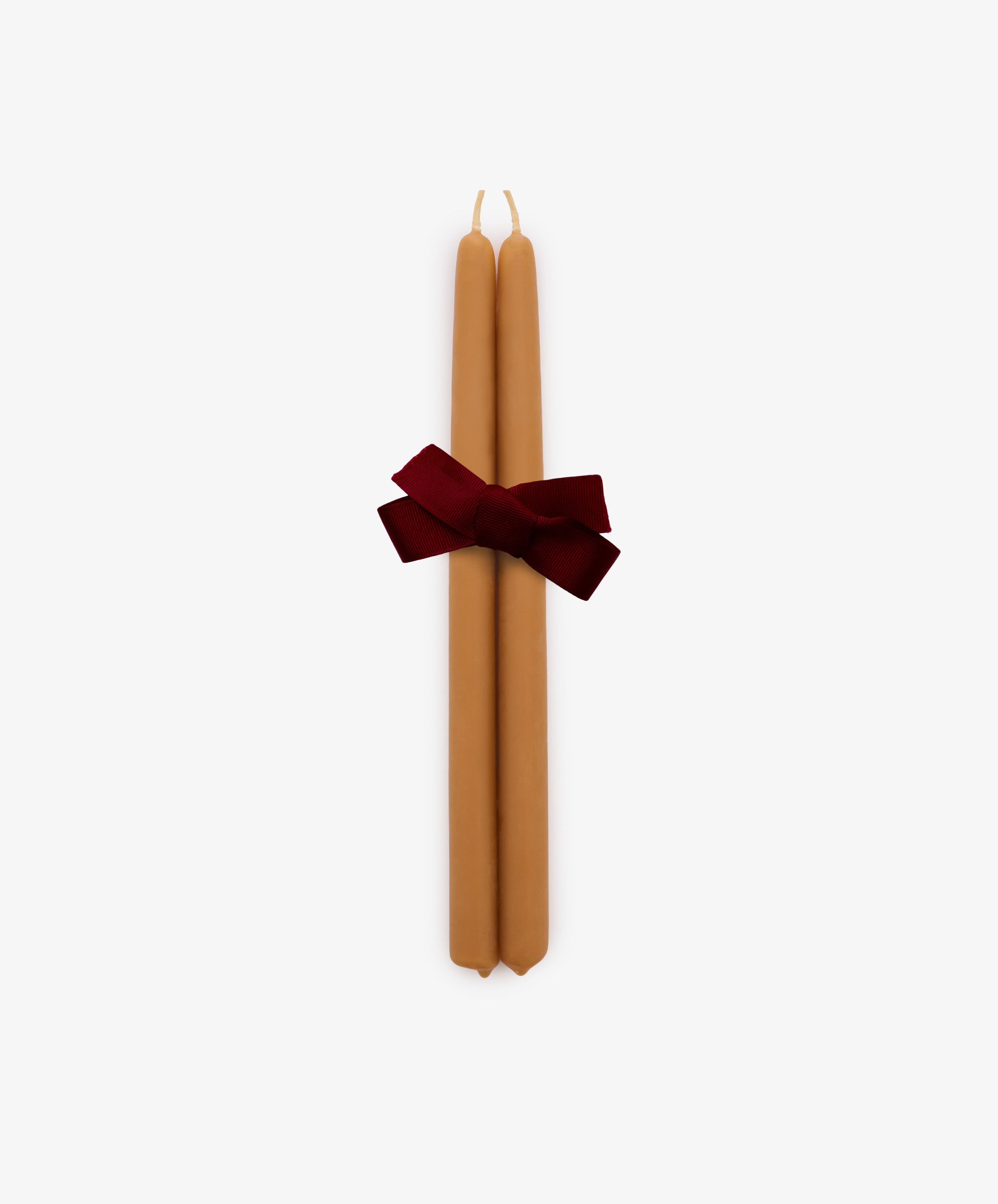 The Tapered Candles, Set of 2, features two hand-dipped tan taper candles tied together with a dark red ribbon and displayed against a plain white background.