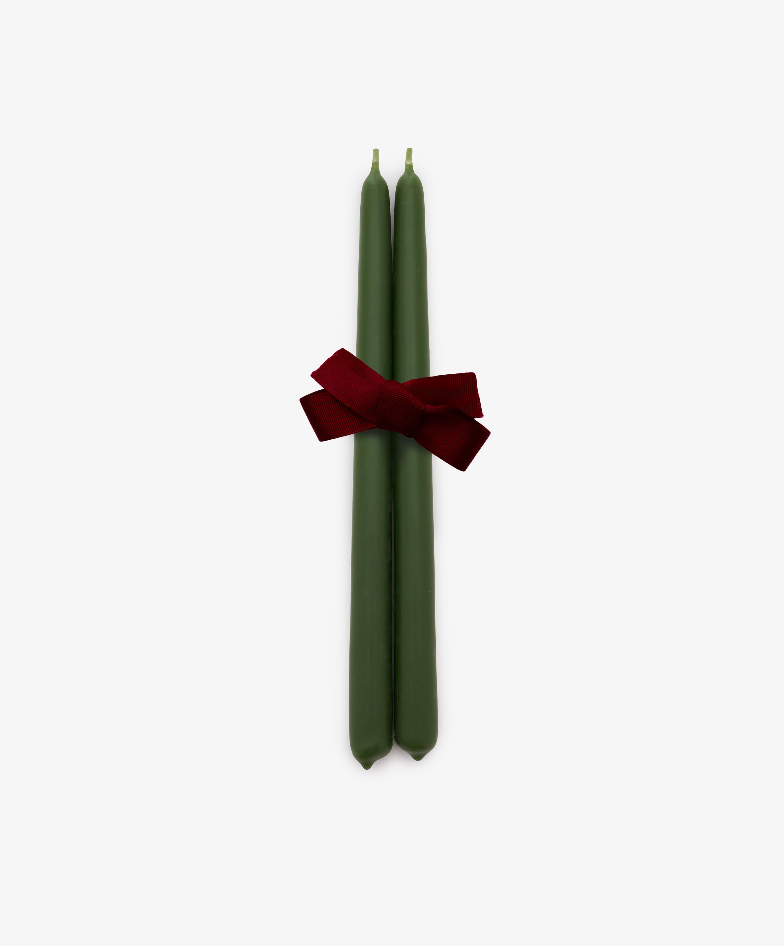 A set of two hand-dipped, mossy green Tapered Candles are tied together with a red ribbon bow and displayed against a plain white background. These elegant candles provide a long burn time, making them ideal for creating a warm and inviting atmosphere.