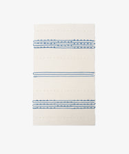 The Gaia Floor Mat, a rectangular cream rug with horizontal blue stripes and dotted patterns, is handwoven from recycled fabric in the Portuguese tradition and shown on a white background.