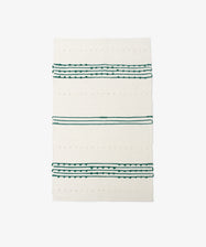 The Gaia Floor Mat is a rectangular white rug featuring green and black horizontal stripes with small textured dots, crafted from recycled fabric in the Portuguese tradition. Shown against a plain white background.