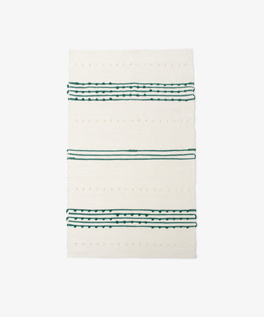 The Gaia Floor Mat is a rectangular white rug featuring green and black horizontal stripes with small textured dots, crafted from recycled fabric in the Portuguese tradition. Shown against a plain white background.