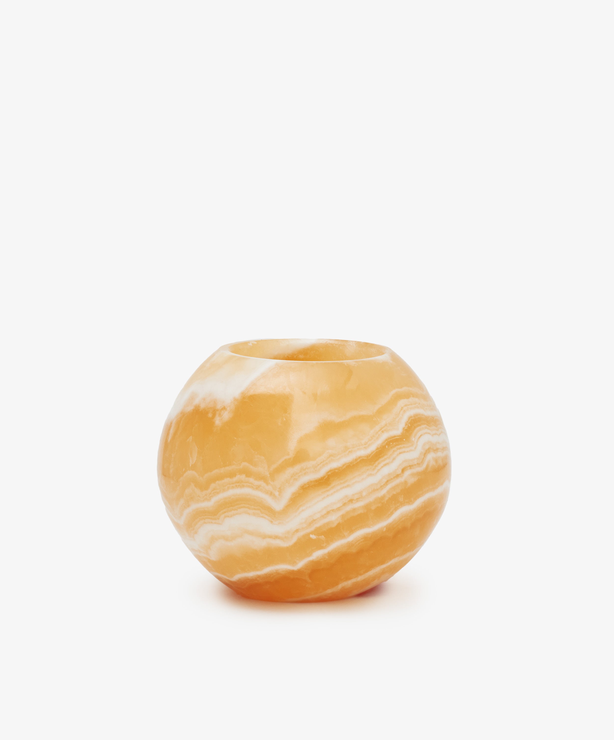 The Akila Candleholder is a round, polished orange onyx vase with natural white banding, inspired by Luxor's artistry and displayed against a plain white background.
