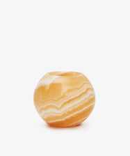 The Akila Candleholder is a round, polished orange onyx vase with natural white banding, inspired by Luxor's artistry and displayed against a plain white background.