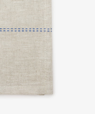 Close-up detail of natural linen napkin with blue stitching detail.