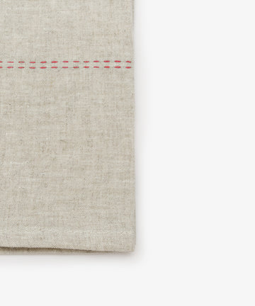 Close-up detail of natural linen napkin with red stitching detail.
