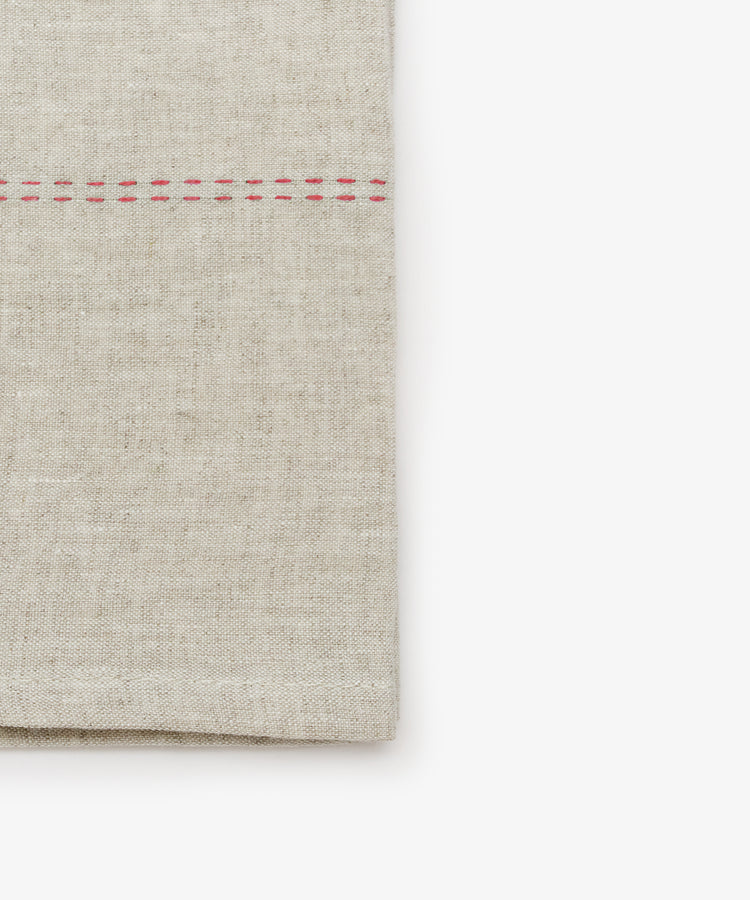 Close-up detail of natural linen napkin with red stitching detail.