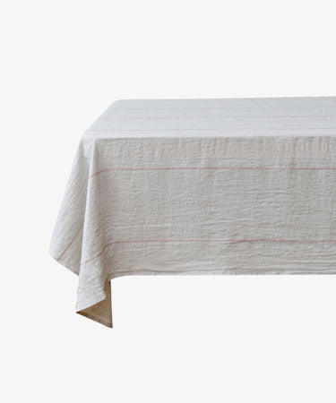 Rythmo Linen Tablecloth. Natural linen cloth with red stitching draped over floating table.