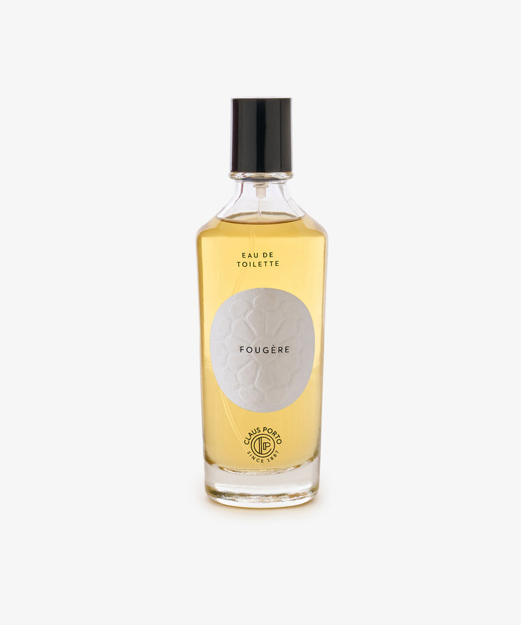A clear glass bottle with light amber liquid, black cap, and a white label reading Fougère Eau de Toilette, evoking pine needle and cedarwood notes.