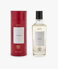 A red cylindrical Claus Porto box sits next to a clear glass bottle of Porto Eau de Toilette with white labels and a fresh citrus scent.
