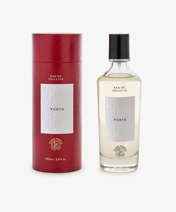 A red cylindrical Claus Porto box sits next to a clear glass bottle of Porto Eau de Toilette with white labels and a fresh citrus scent.
