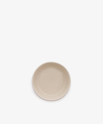 A plain, round, beige ceramic plate is centered on a white background, contrasting with a classic blue and white stripe dish like the Betty Dip Dish.