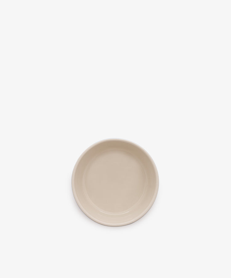A plain, round, beige ceramic plate is centered on a white background, contrasting with a classic blue and white stripe dish like the Betty Dip Dish.