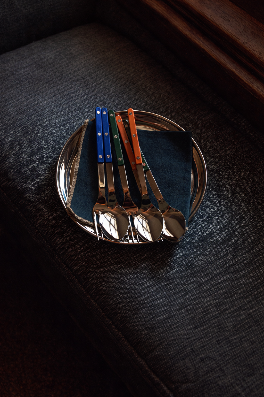 Set of four silver spoons with colored handles on a dark surface