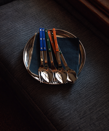 Set of four silver spoons with colored handles on a dark surface