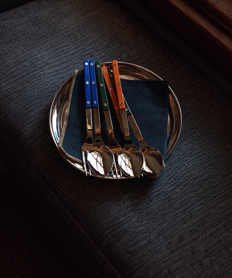 Set of four silver spoons with colored handles on a dark surface