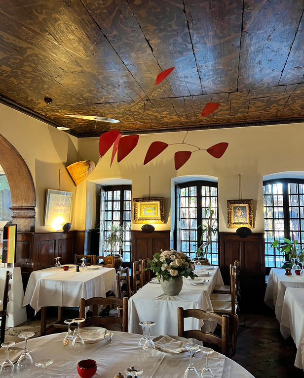 Elegant dining room with white tablecloths, wooden chairs, framed art, and a red mobile hanging from the ceiling