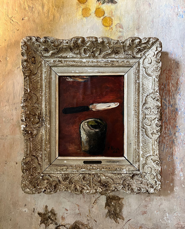 Framed painting of a knife and cup against a dark background, in an ornate carved frame