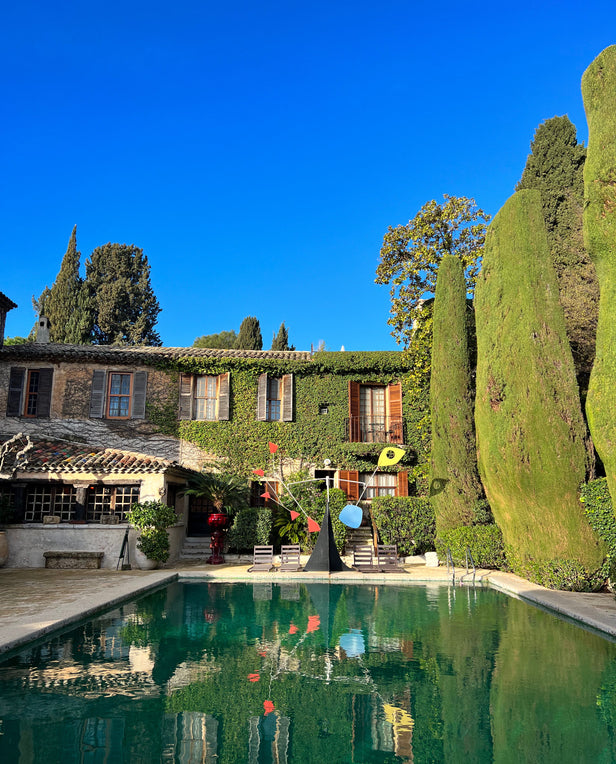 Vine-covered house with tall cypress trees and a swimming pool in front under a clear blue sky