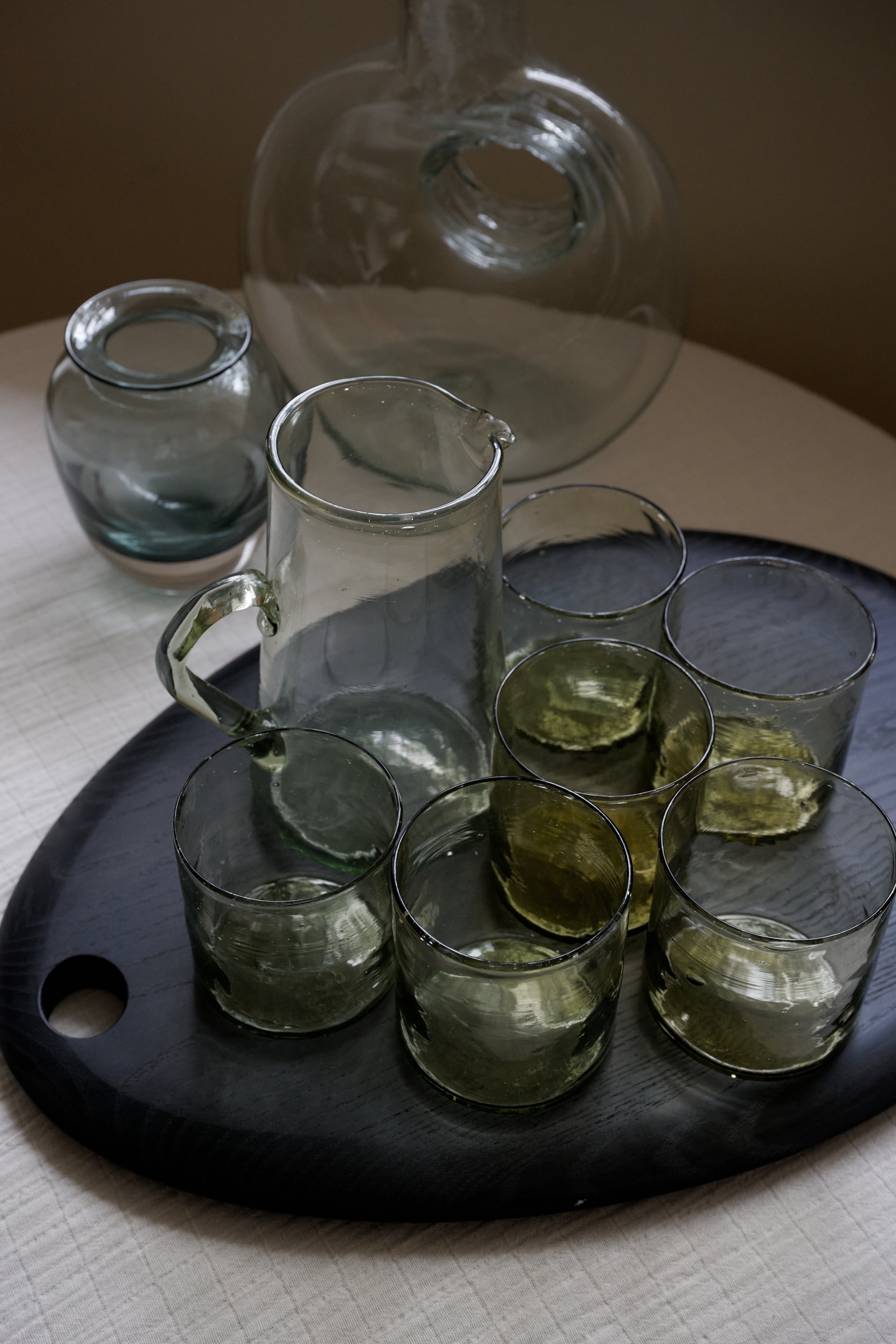 Set of clear glass tumblers and a pitcher on a dark tray with a blurred background