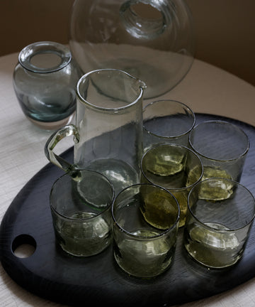 Set of clear glass tumblers and a pitcher on a dark tray with a blurred background