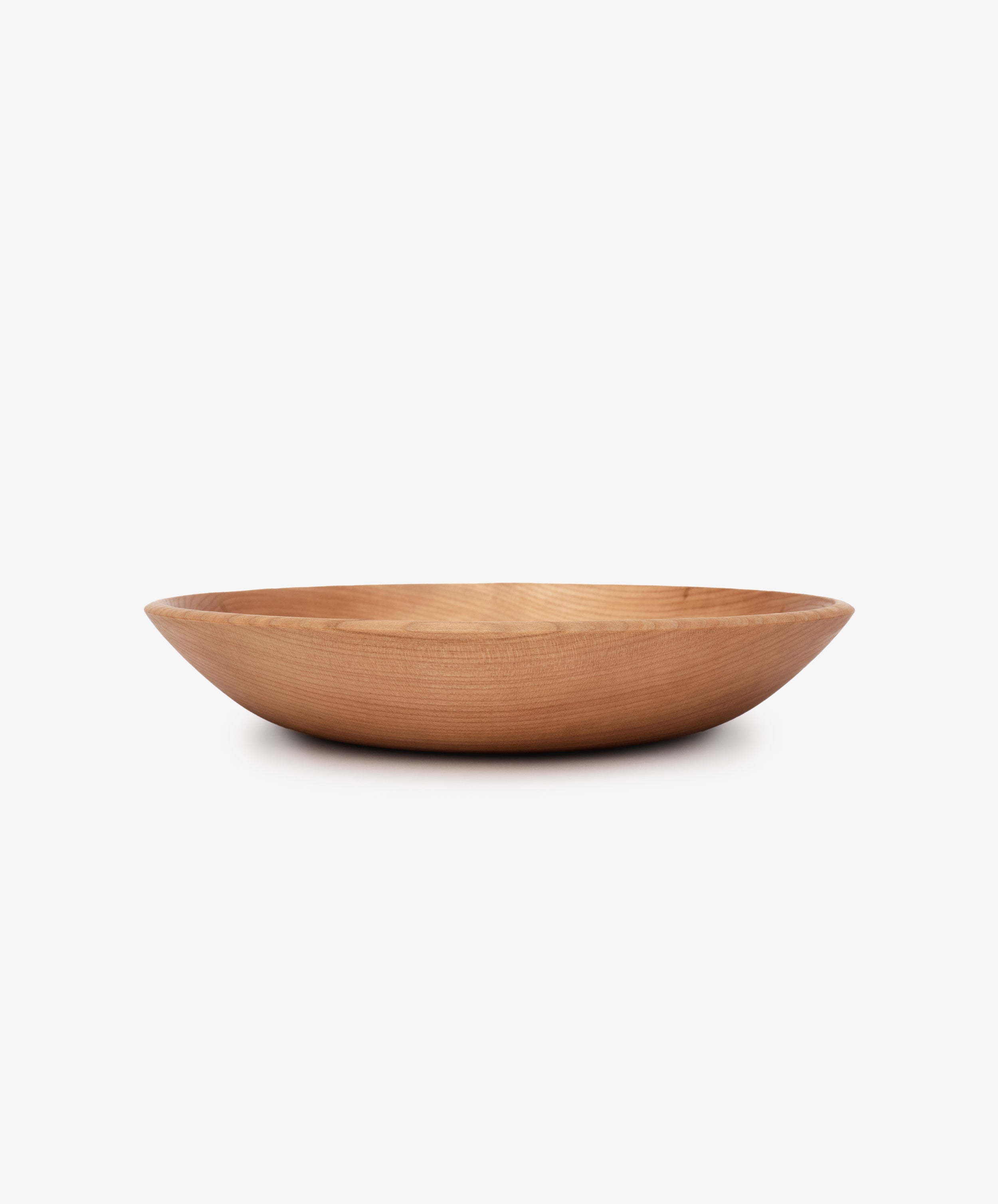 The August Wood Serving Bowl is a shallow, round bowl made from American dark cherry wood with smooth sides, shown against a plain white background.
