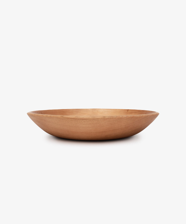 The August Wood Serving Bowl is a shallow, round bowl made from American dark cherry wood with smooth sides, shown against a plain white background.