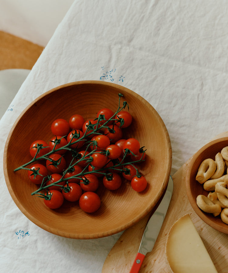 Wooden bowl with cherry tomatoes on a tablecloth with a knife and cheese.