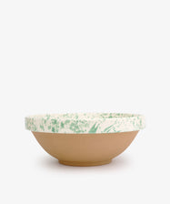 The Rita Bowl Splatter is a shallow ceramic bowl with a matte tan base and white rim, accented by green splatter patterns, shown on a plain white background.