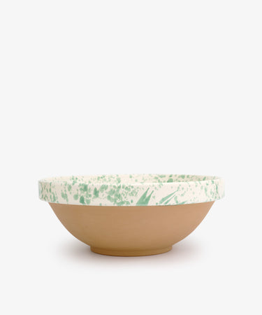The Rita Bowl Splatter is a shallow ceramic bowl with a matte tan base and white rim, accented by green splatter patterns, shown on a plain white background.