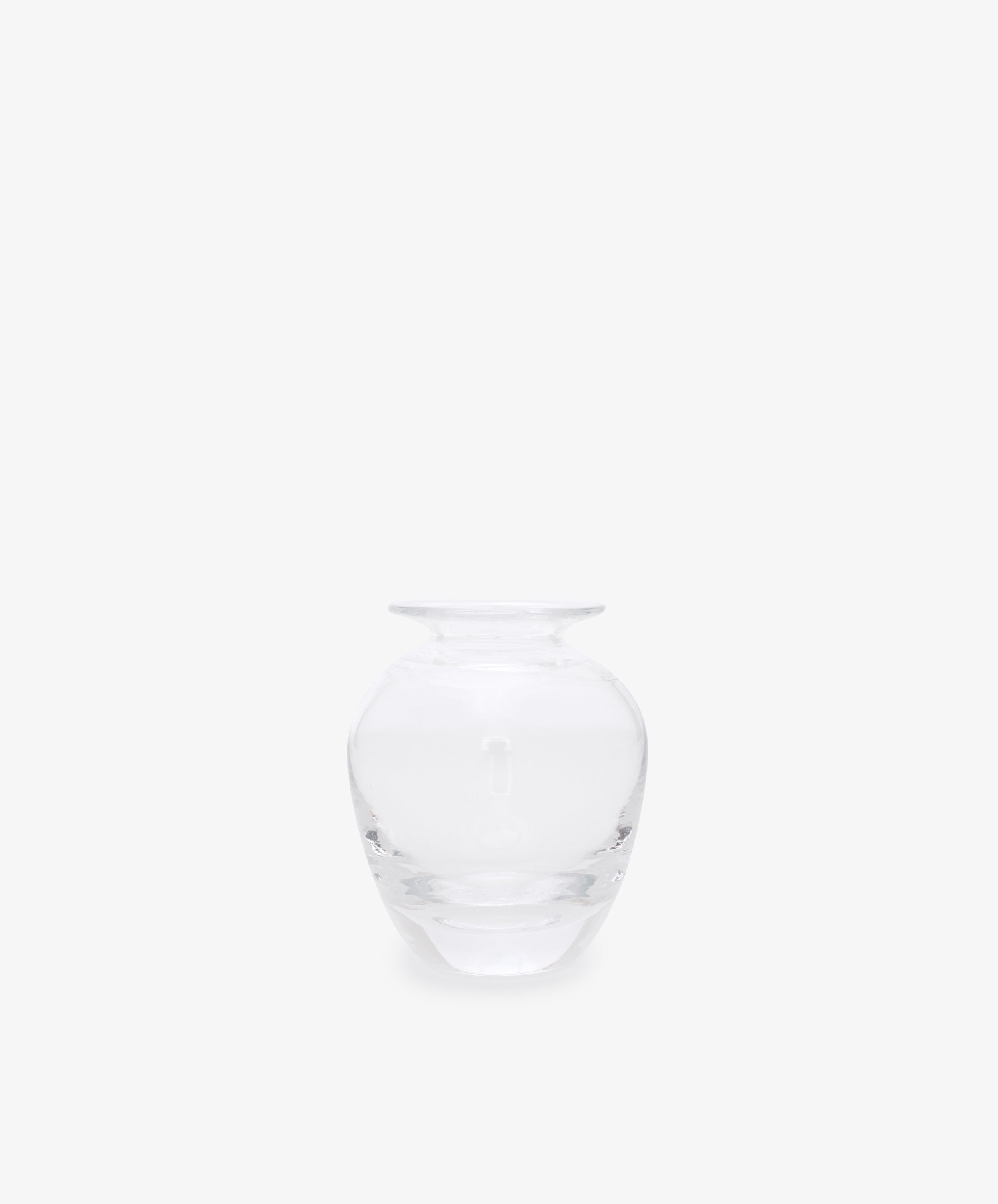 The Gem Bud Vase is a clear glass vase with a wide, round body and short, narrow neck, inspired by hand-blown bud vases from the South of France. It is showcased against a plain white background.