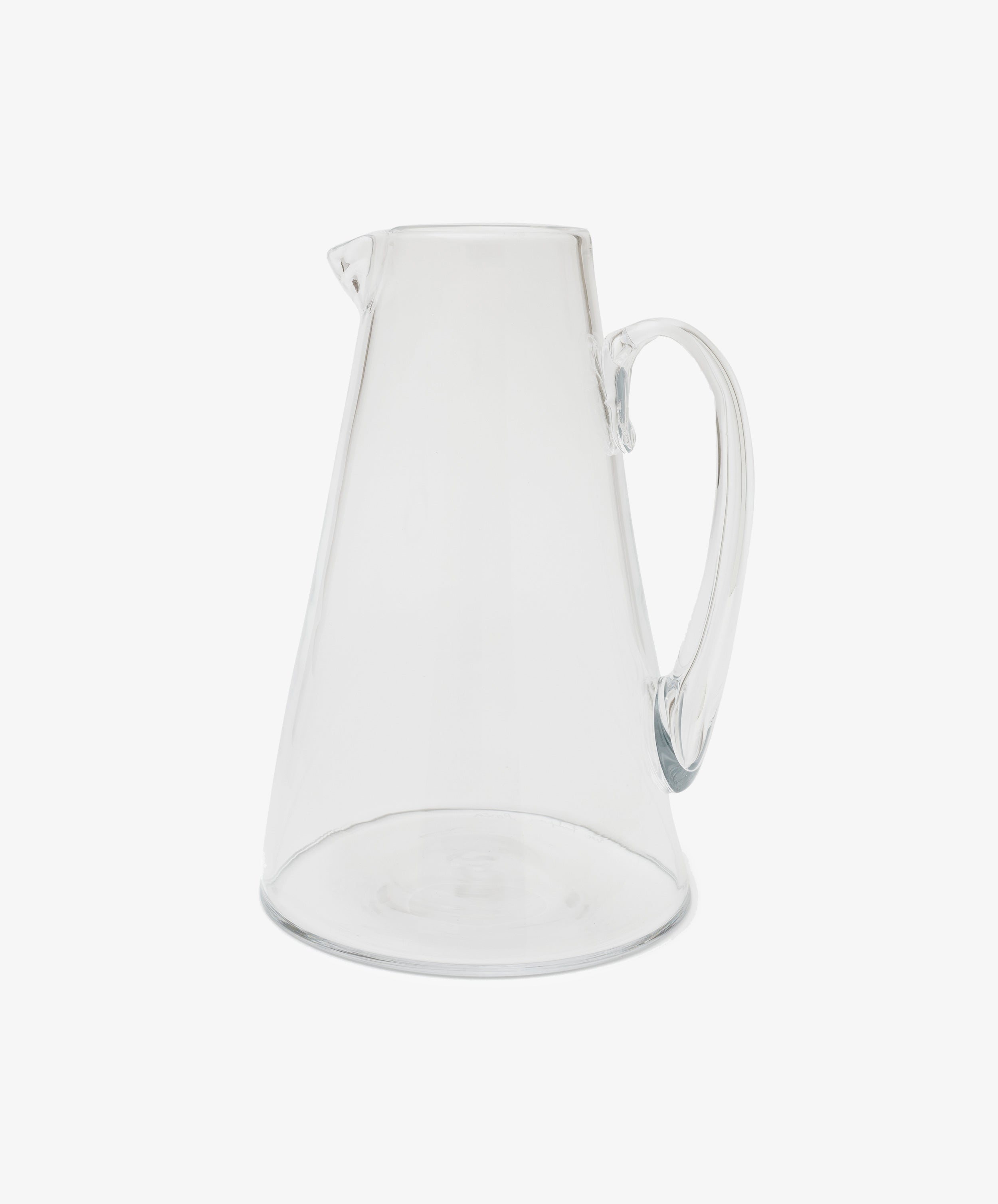 Handmade in the South of France, the Gemma Jug is a clear glass pitcher with crystal transparency, wide base, narrow top, small spout, and curved handle—beautifully photographed on a plain white background.