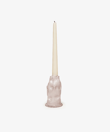 The Pellizco Candleholder, hand-moulded in the shape of a hand, holds a white taper candle upright against a plain white background.
