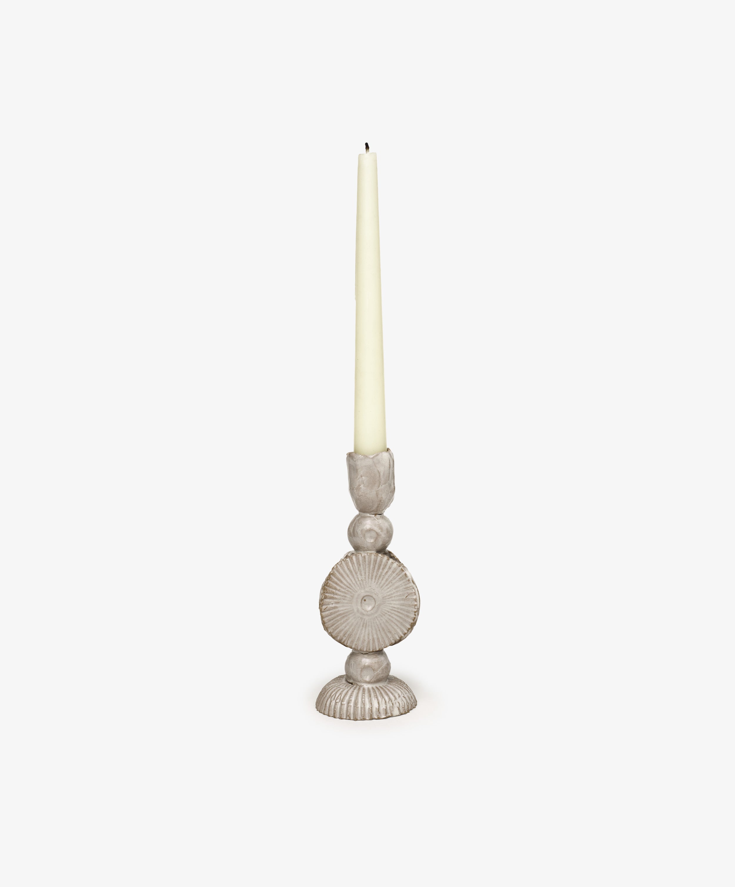 A tall, unlit cream taper candle rests in the sculptural Circulo Candleholder, a hand-moulded beige piece with ornate details, set against a plain white background.