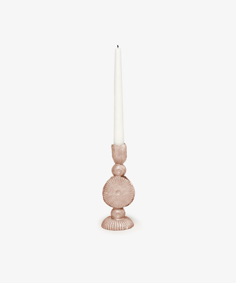A white taper candle sits in the Circulo Candleholder—a round, pink handmade holder with textured patterns—set against a plain white background.