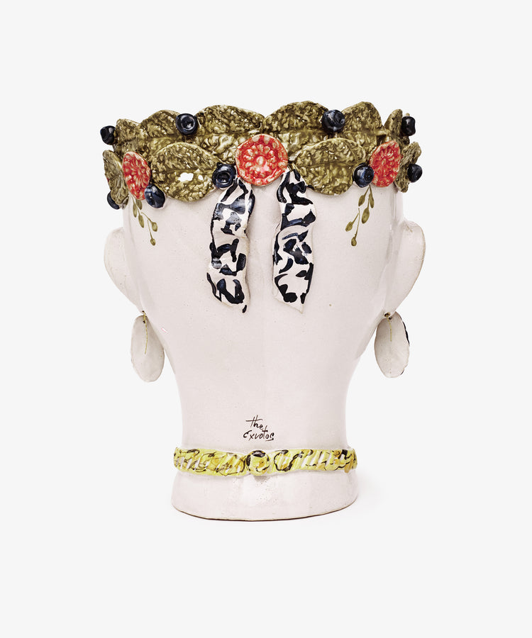 The Testa di Moro, Arandano is a ceramic bust viewed from behind, featuring a leafy wreath with berries, black-and-white ribbon, and yellow necklace—a sculptural home accent inspired by classic Testa di Moro heads.