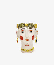 Testa di Moro, Alfonsina: A ceramic vase shaped like a womans head with red cheeks, gold earrings, a necklace, and a green leaf crown with yellow flowers. Sculptural and unique homeware. Displayed on a plain white background.