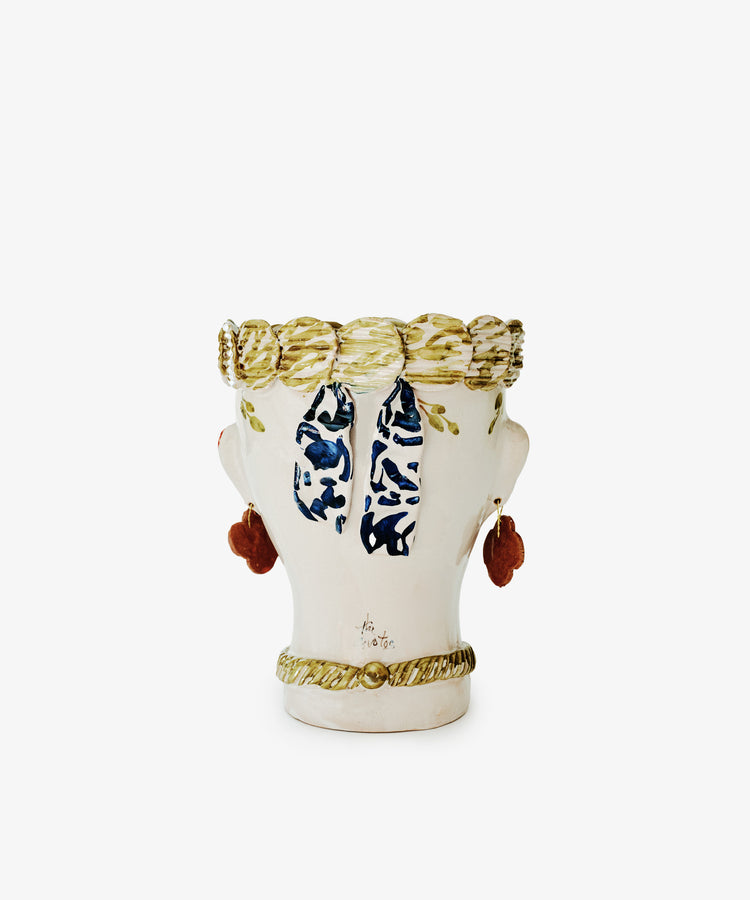 The Cabeza Recipiente, Biloba is a ceramic vase shaped like a human head with painted hair, earrings, and a scarf. This unique handmade decor piece is shown from the back against a plain white background.