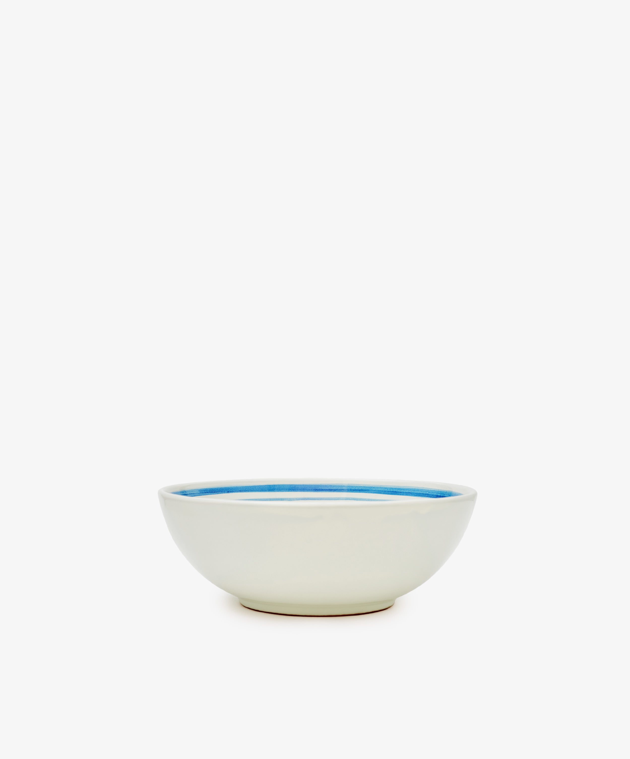 The Folk Cereal Bowl, Jester features a white ceramic body with a hand-painted blue interior rim by an Italian ceramist, adding whimsical charm to your table. Shown on a plain white background.